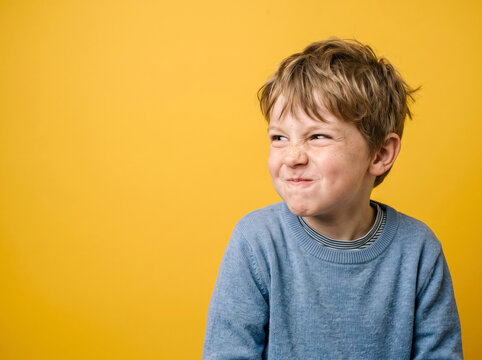 Boy making funny face with a wrinkled nose against a bright yellow background