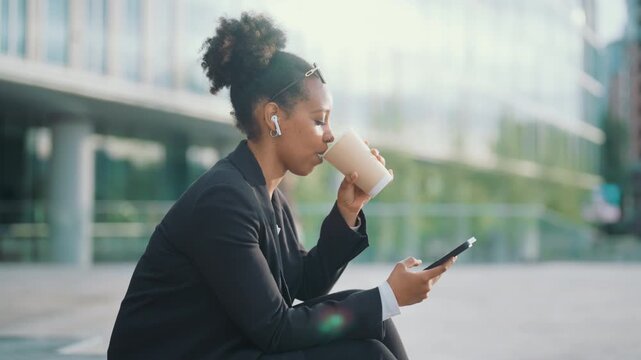 Happy townswoman calling by mobile, listening sound by earphones, drink coffee. Good morning in metropolis, businesswoman discussing working asks by phone outdoors, modern technology for work and rest