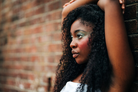 Thoughtful young woman with curly hair by brick wall