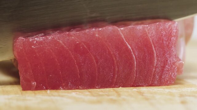 Professional chef slicing fresh raw red tuna fillet for sashimi on wooden board.