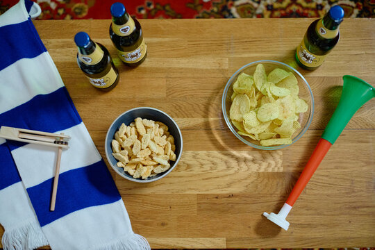 Beer bottles, snacks, scarf, and fan horn lying on wooden table, representing preparation for watching soccer match. Image suitable for sports bar promotion or game day marketing, high angle view