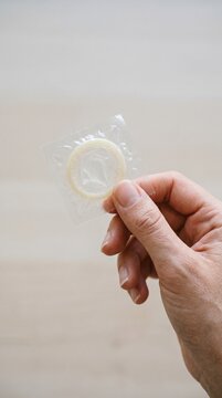 Female hand holding a condom wrapper in a neutral setting  