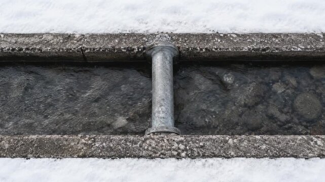 Overhead View of Flowing Meltwater in Snow Melting Roadside Drainage Channel