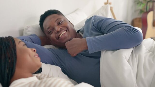 African American couple lying down together on bed in bedroom at home. 