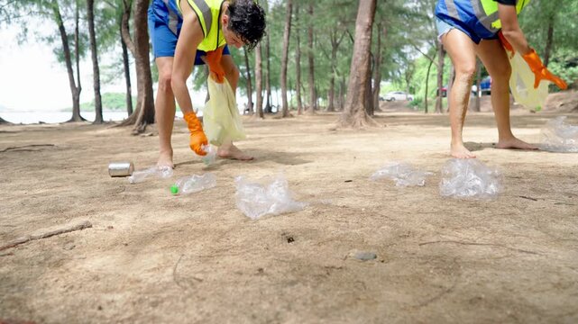 Close up of two volunteers collect plastic bottles and trash on sandy beach. 