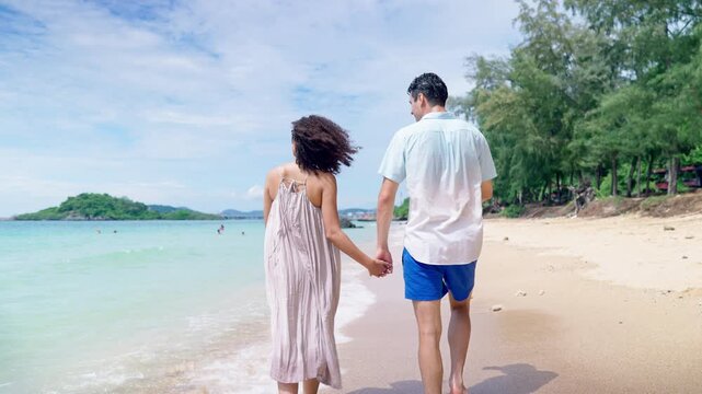Caucasian young man and Latina girlfriend walking on sandy beach together.
