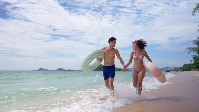 Young loving couple holding swim rings and run along the sandy beach. 