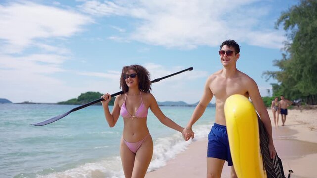 Loving couple carrying a paddleboard and walk along the sandy beach. 