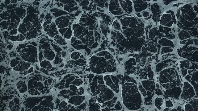 Aerial view of dark wastewater with foamy surface patterns inside an industrial treatment plant, representing pollution control, water purification processes, and environmental management. 4k.
