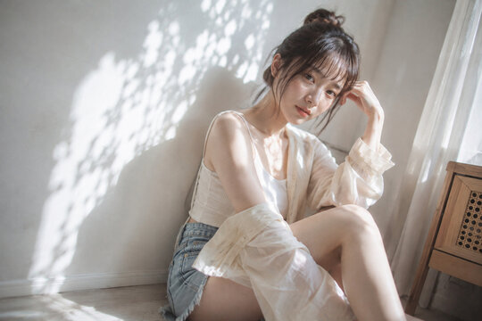 窓辺で膝を抱えて光を受ける女性の室内ポートレート