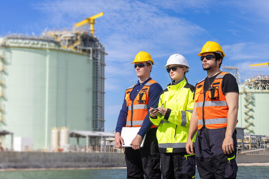 lng plant engineers team standing together at terminal storage facility, liquefied natural gas plant workers in safety gear at industrial site, energy industry professionals inspecting storage tanks