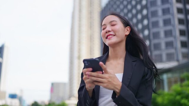 Asian young businesswoman chatting on smartphone while standing in city. 