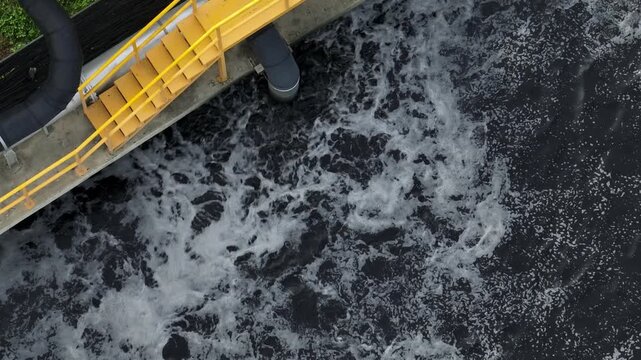 Aerial photography of black wastewater undergoing treatment with bubbling foam and industrial equipment, representing water quality improvement, ecosystem protection, sustainable wastewater solutions.