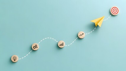Fototapeta premium Yellow Paper Origami Flying Along Dotted Path Over Wooden Milestone Icons Toward Target Bullseye