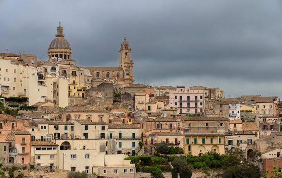 panoramic view of a historic Italian town featuring baroque architecture and church spires against a backdrop of stormy clouds