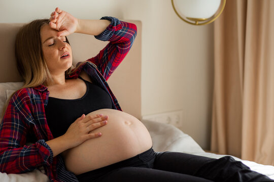 Pregnant woman in late pregnancy resting on bed and holding her belly during labor discomfort