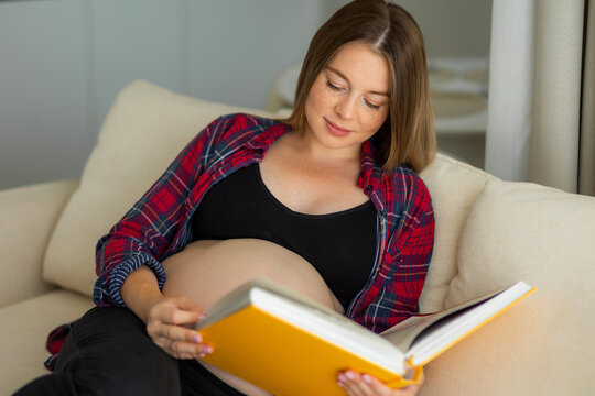 Pregnant woman reading a book on a cozy couch, relaxed expectant mother preparing for baby