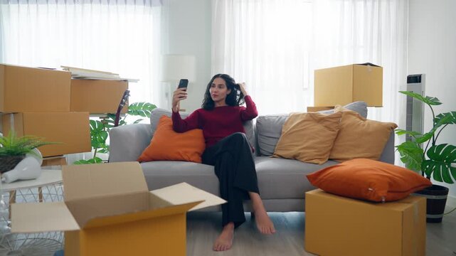 Young Hispanic woman using phone video call while moving into a new home. 