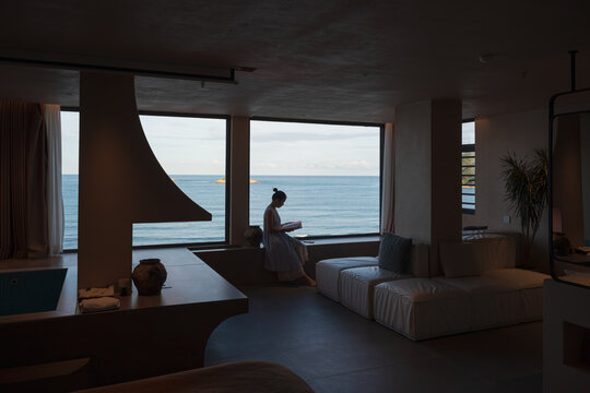 The woman reading by a window overlooking the ocean