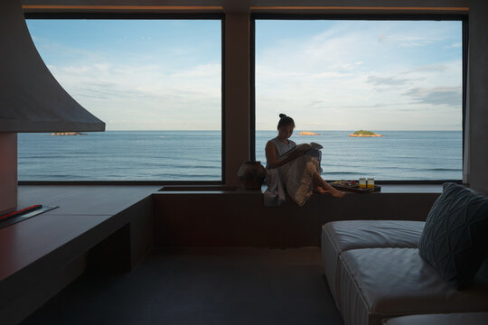 The woman reading by a window overlooking the ocean