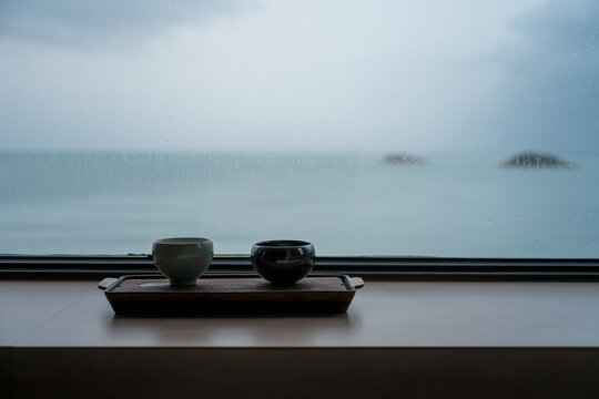 On a rainy day, two ceramic teacups are placed on a tea tray by the window.