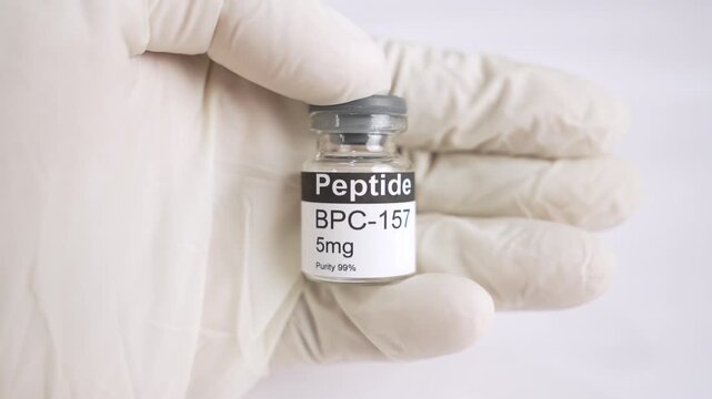 Gloved hand holding an BPC 157 peptide vial