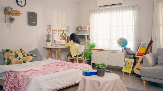 African American teenage girl sit at table drawing on paper in a cozy house. 