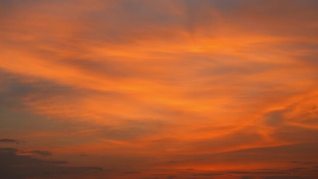 A sunset sky timelapse video featuring layered altostratus clouds and thin cirrostratus clouds glowing in warm orange and amber light, with darker low clouds along the horizon creating a evening. 4k.
