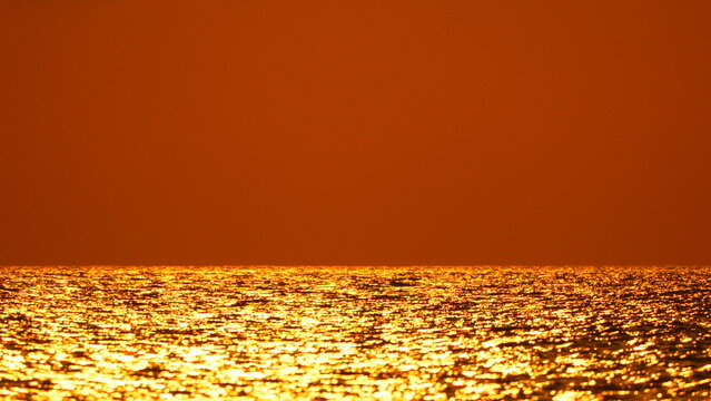 Sunset ocean water shimmering golden waves at sea under a vast orange sky with plenty of copy space