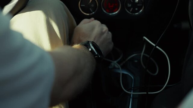 Close-up overhead view of man's hand with watch shifting gear stick into first gear on manual transmission inside car interior with dashboard visible. Automotive driving concept for vehicle and automo