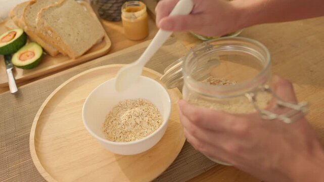 Close up of woman preparing healthy bowl of oatmeal with milk in home kitchen. 