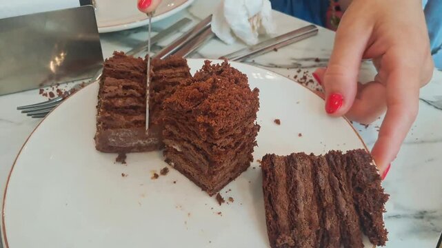 a person cutting a slice of chocolate cake on a marble table with a knife and fork