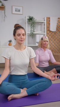 Caucasian young woman practicing yoga with senior mother in cozy house. 