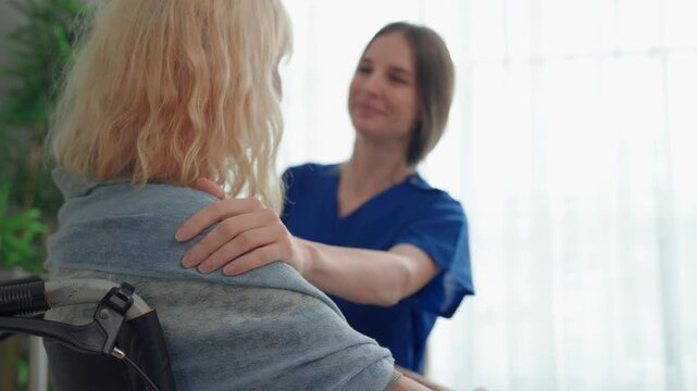 Caucasian caregiver assisting senior woman in wheelchair at nursing home. 