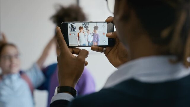 African American male teacher using smartphone to record diverse school children posing in art gallery. Footage is ideal for educational marketing and museum promotion campaigns