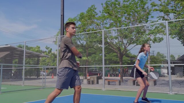 Young man and woman playing mixed doubles pickleball on outdoor court. 