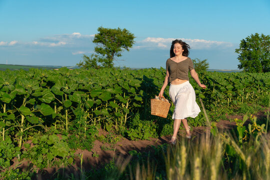 Happy young woman walking through sunflower field carrying wicker basket