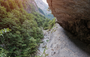Fototapeta premium Narrow hiking path following the towering cliffs and lush forests of a dramatic Balkan gorge with a river below