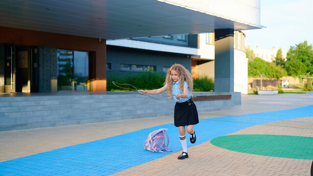 A happy schoolgirl skipping rope in front of her school building
