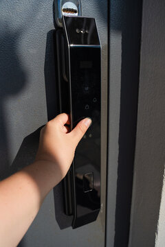 Fingerprint entry of the black smart lock on the gray metal door. A woman's hand puts her finger on the reader