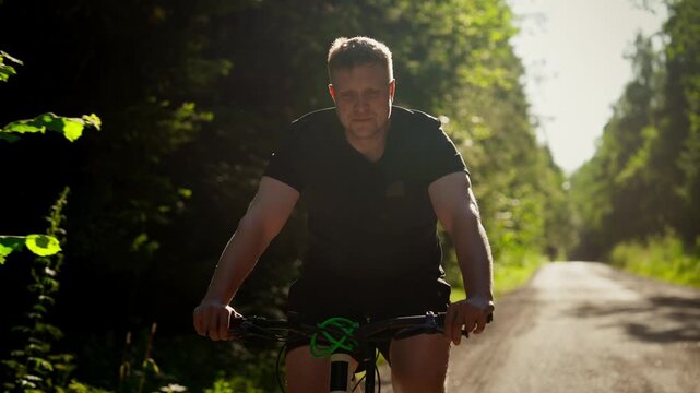 Man cycling along a sunlit forest road, enjoying an active outdoor ride surrounded by lush green trees and peaceful nature on a bright summer day