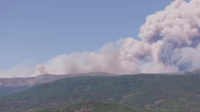 Stationary drone footage at 70mm with a lateral pan revealing the enormous scale of a pyrocumulus cloud rising above the mountains of the Ti&eacute;tar Valley.