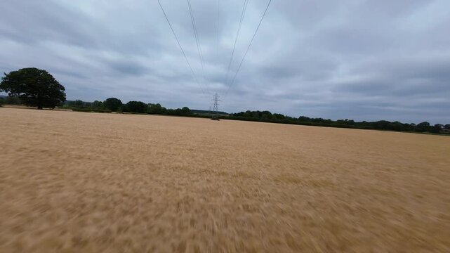 FPV drone fast low flight skim over rural farmland near high voltage power lines and pylons UK