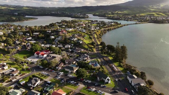 Aerial view of Raglan on New Zealand&rsquo;s North Island, showing the coastal town, waterfront, harbour and surrounding green hills during golden hour.