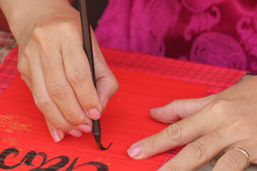 Close-up of a female calligrapher hands writing traditional greetings with black ink on a red paper scroll for Tet holiday, Ho Chi Minh City, Vietnam. © d_odin