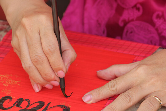Close-up of a female calligrapher hands writing traditional greetings with black ink on a red paper scroll for Tet holiday, Ho Chi Minh City, Vietnam.