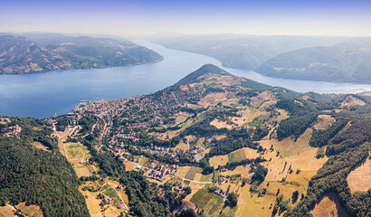 Fototapeta premium Bright summer aerial panorama of a riverside town nestled among rolling green hills along a wide Danube river winding through forested valleys. Travel concept.