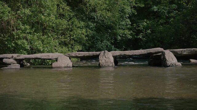 Tarr Steps with reflections of trees shimmering in the river below. The peaceful setting and balanced framing provide a timeless view of this historic landmark in Exmoor National Park.
