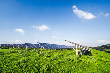 Photovoltaic solar panel arrays are installed on a lush green field under a clear blue sky, demonstrating renewable energy infrastructure. © tai