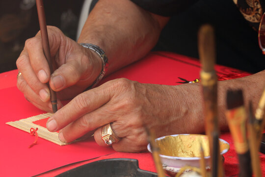Close-up of a master calligrapher hands writing traditional greetings with gold ink on a red paper scroll, Ho Chi Minh City, Vietnam.